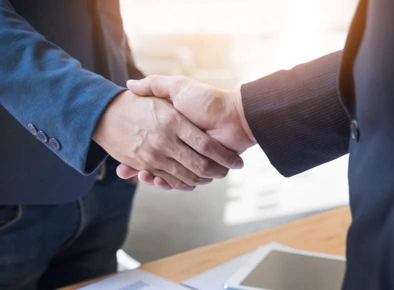 A lawyer and client shaking hands across a desk with legal items